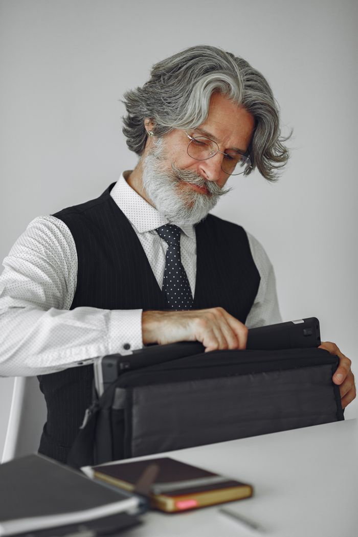 Stylish senior businessman with gray hair organizing papers into a bag in an office setting.