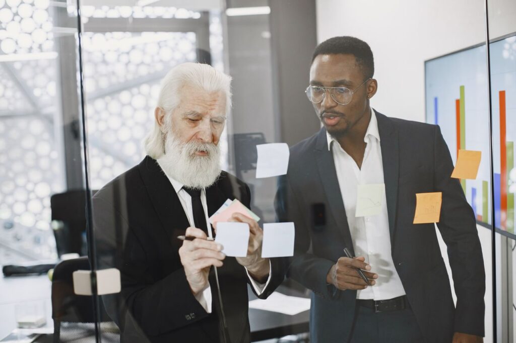 Two businessmen collaborating on a project in a modern office using sticky notes for brainstorming.
